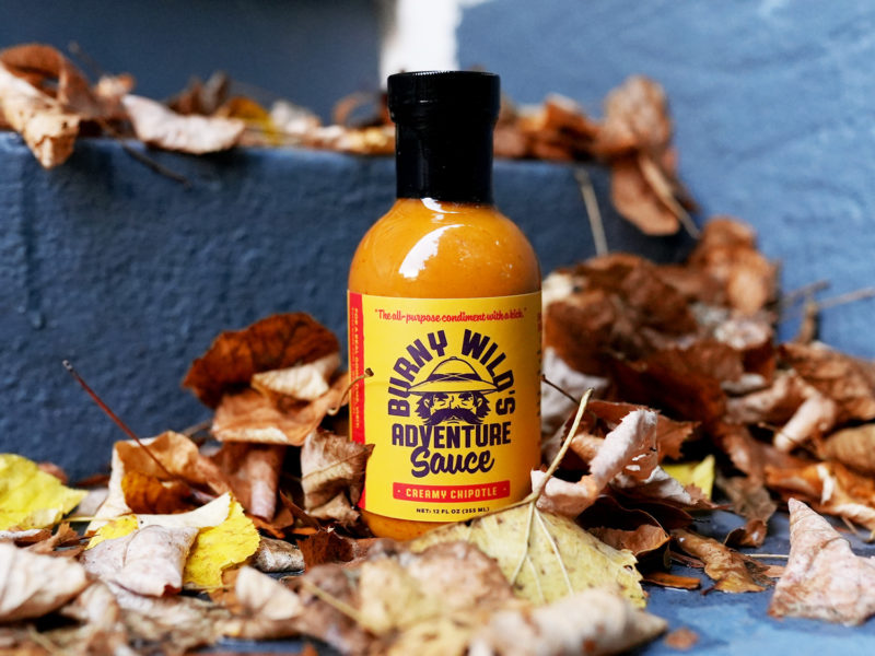 Bottle of Burny Wild's Adventure Sauce amongst a pile of leaves