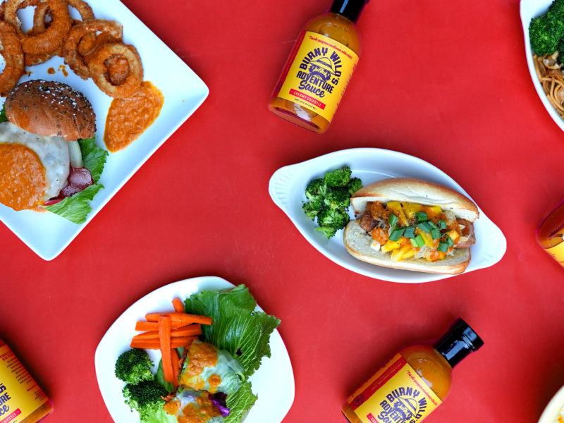 Bottles of Burny Wild's Adventure Sauce amongst hot dogs, pad thai, burgers and more.
