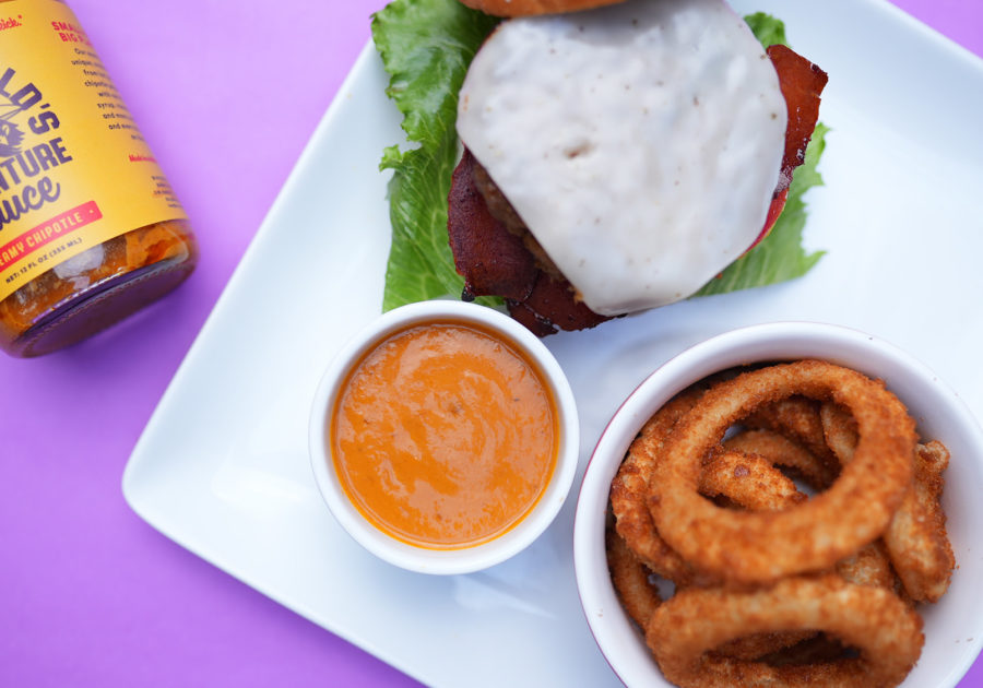 Bottle of Burny Wild's Adventure Sauce paired with a burger and onion rings